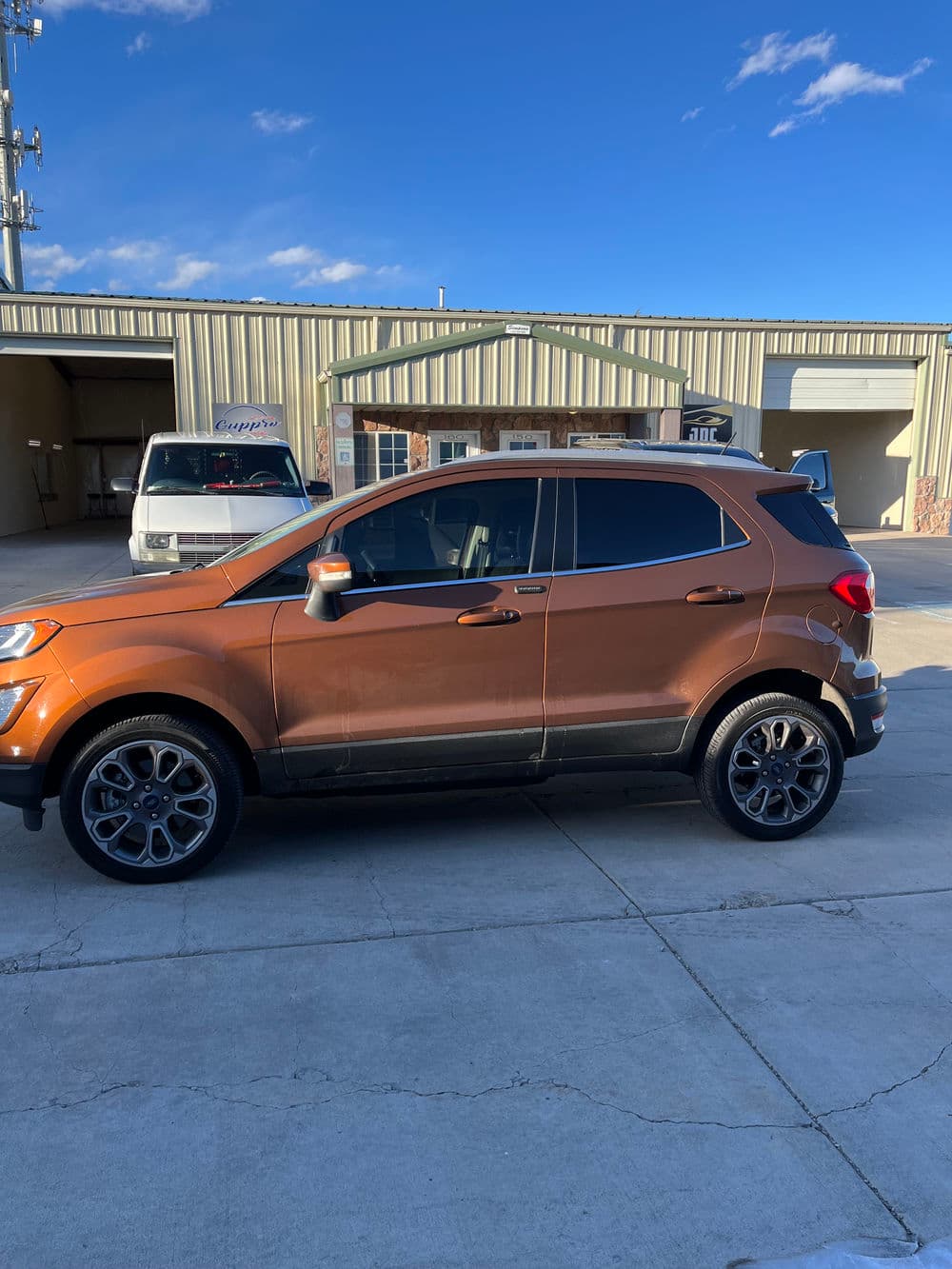 Orange SUV parked outside a building under blue sky with clouds.