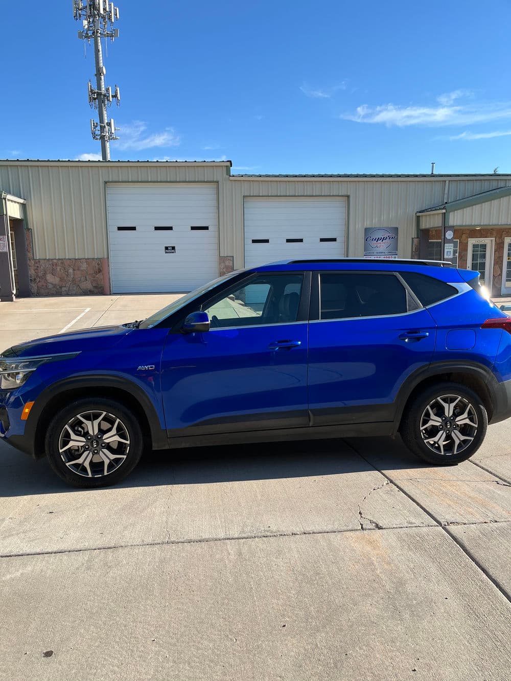 Blue SUV parked in front of a building with a clear blue sky and garage doors.